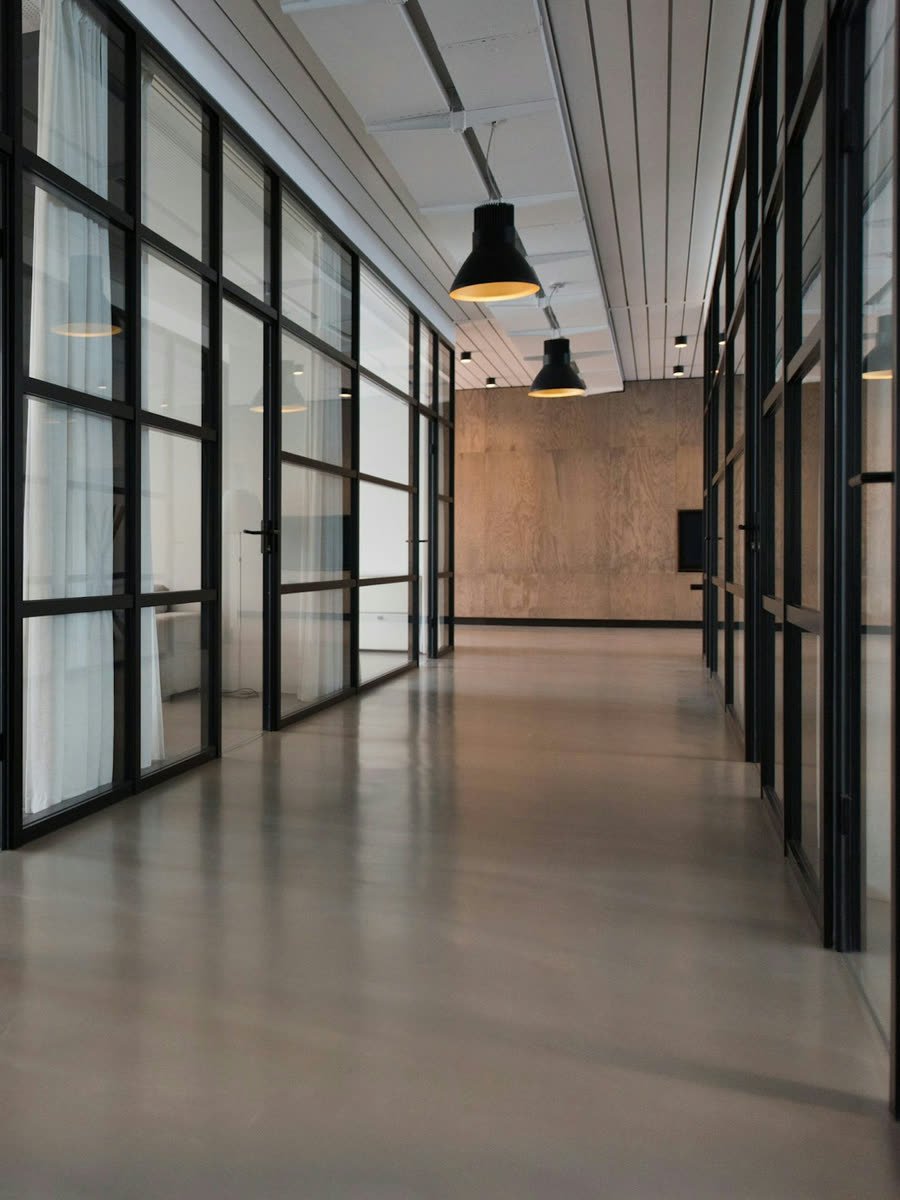 An office corridor of glass-partitioned rooms, lit after hours.