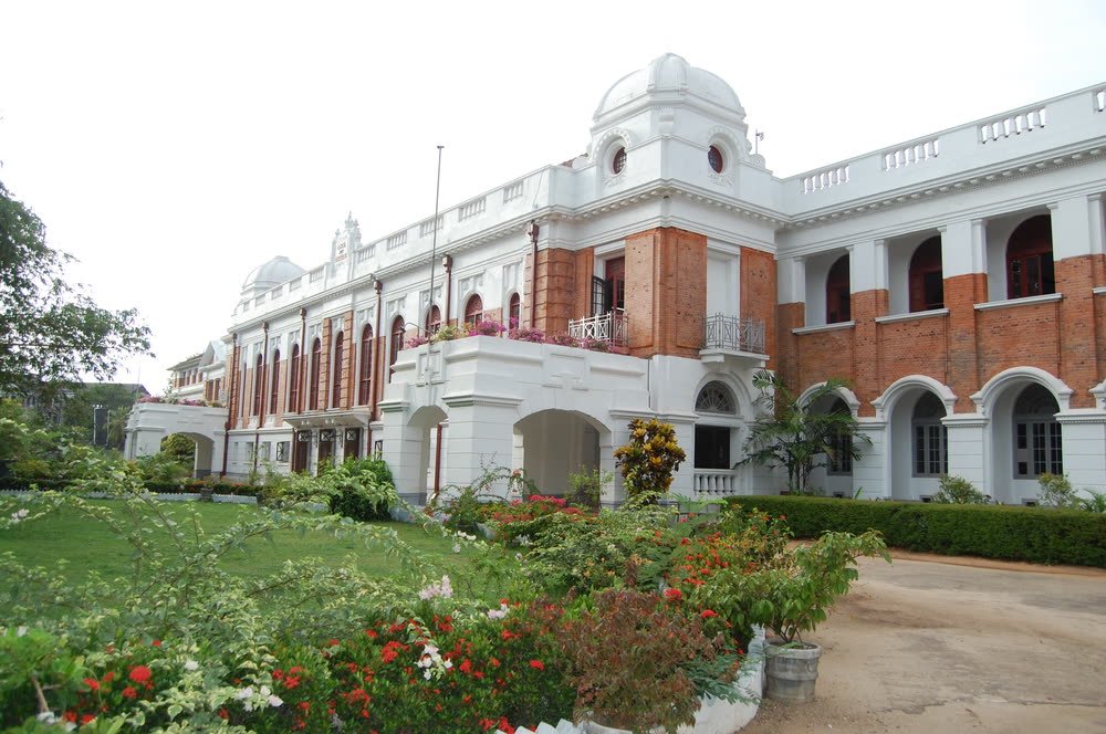 The white colonial main building of Royal College, Colombo, behind a flowering garden.